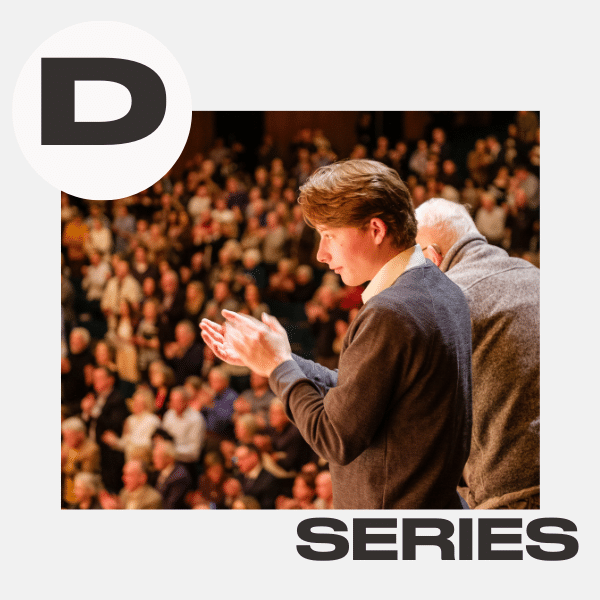 A young man stands on stage clapping, facing an audience of people in a large hall. The letter D is in a white circle at the top left, and the word SERIES is at the bottom right.