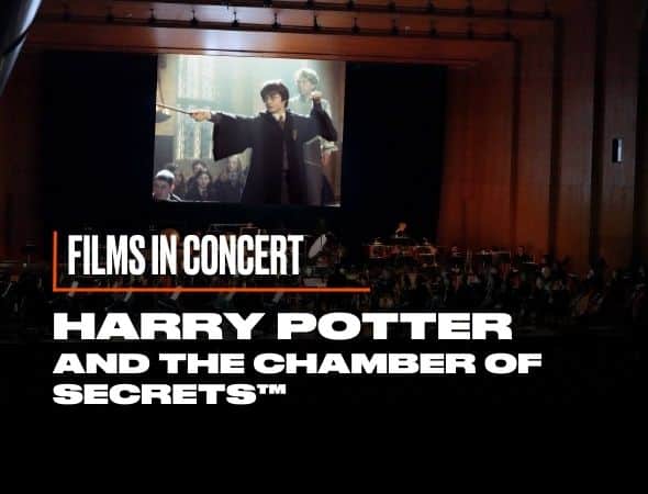 A concert hall features a large screen displaying a scene from Harry Potter and the Chamber of Secrets, showing a character pointing a wand. Below the screen, an orchestra is performing. The text reads, Films in Concert: Harry Potter and the Chamber of Secrets.