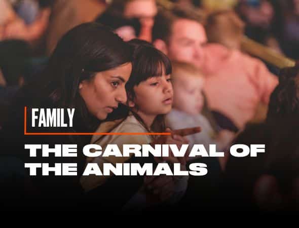 A woman and a child sit together, focused on something in front of them. The overlay text reads, FAMILY The Carnival of the Animals. The setting appears to be a crowded indoor event.