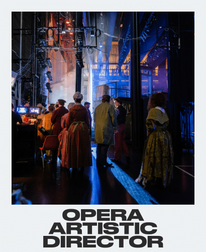 Backstage at an opera, performers in period costumes gather under dramatic lighting, with stage equipment and a lit set visible in the background. Text at the bottom reads Opera Artistic Director.