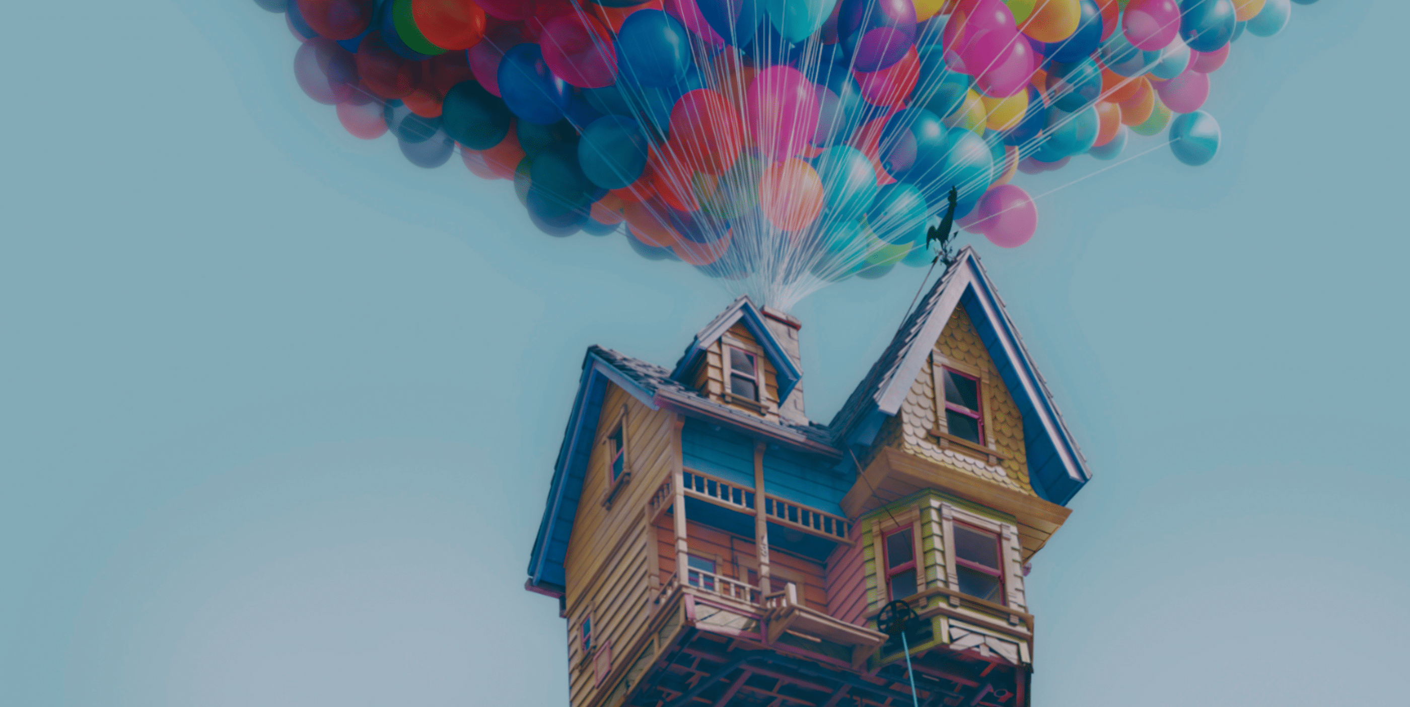 A wooden house is floating in the sky, lifted by hundreds of colorful balloons attached to its roof against a clear blue sky.