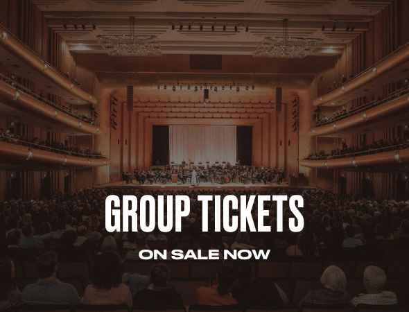 A concert hall filled with an audience facing a lit stage with an orchestra. Large white text in the foreground reads: GROUP TICKETS ON SALE NOW.