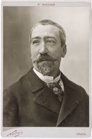 Middle-aged man with very short greying hair, moustache, and beard, looking slightly away from the camera.
