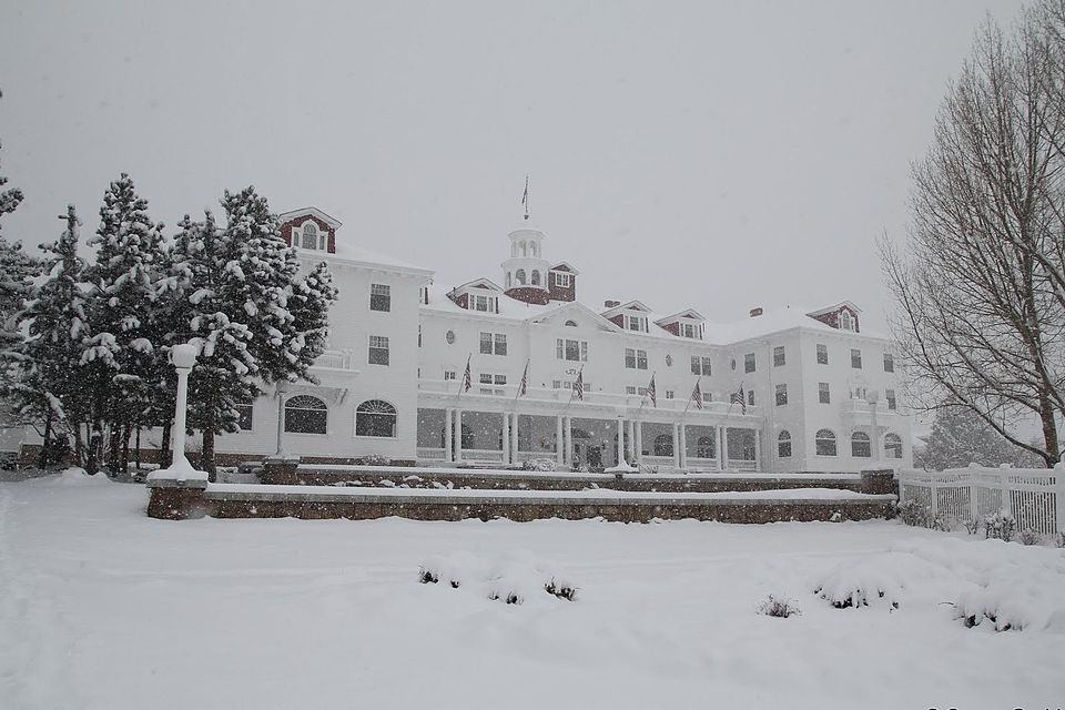 A white colonial revival hotel covered in snow stands against a light grey sky. Surrounding lawn and trees are also white with snow.